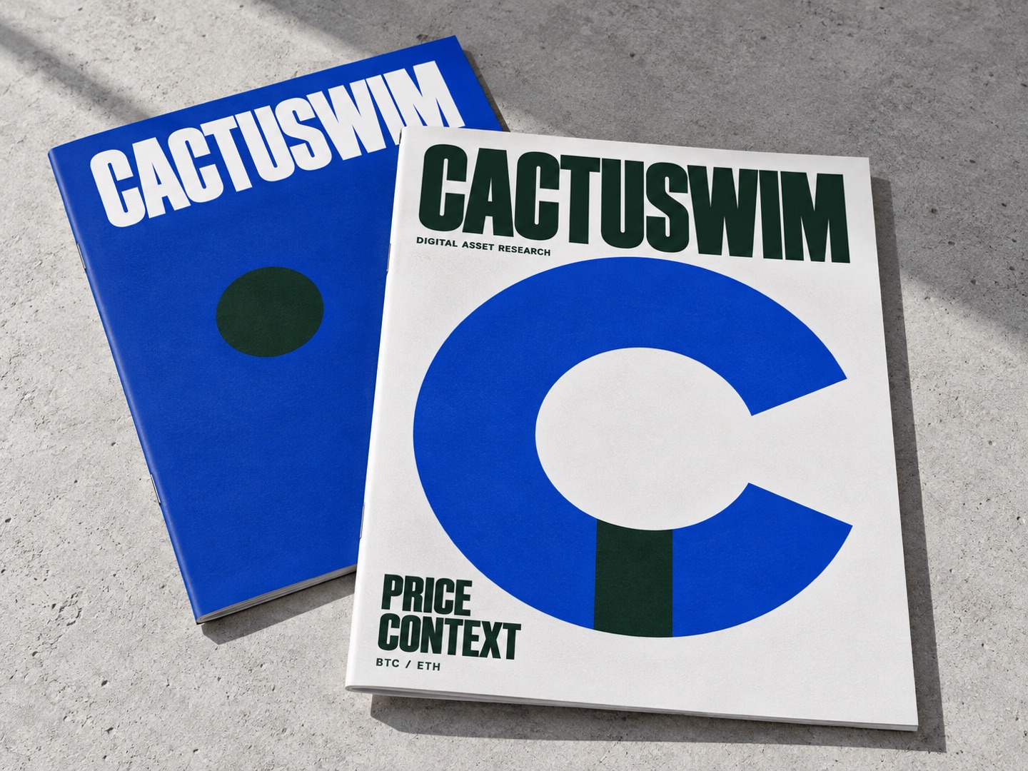 An illustrative pair of thin CACTUSWIM research magazines in cobalt and forest, with PRICE / CONTEXT and BTC / ETH on the cover.